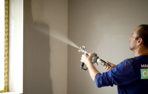 Professionel maler sprøjtespartler en væg.